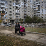 
              A couple pushing a baby stroller walks past a building damaged by a Russian missile in Mykolaiv, Sunday, Oct. 23, 2022. (AP Photo/Emilio Morenatti)
            