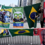 
              A man sells flags during general elections in Sao Paulo, Brazil, Sunday, Oct. 2, 2022. For sale are Brazil national flags and of Presidential candidates, the incumbent Jair Bolsoaro and former president Luiz Inacio "Lula" da silva, (AP Photo/Andre Penner)
            