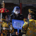 
              A security guard wearing a face shield and mask asks visitors wearing the emperor and empress costumes to scan their traveling code before entering to the Forbidden City during the opening ceremony of the 20th National Congress of China's ruling Communist Party in Beijing, China on Sunday, Oct. 16, 2022. The overarching theme emerging from China's ongoing Communist Party congress is one of continuity, not change. The weeklong meeting is expected to reappoint Xi Jinping as leader, reaffirm a commitment to his policies for the next five years and possibly elevate his status even further as one of the most powerful leaders in China's modern history. (AP Photo/Andy Wong)
            
