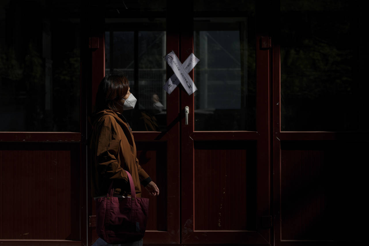 A woman wearing a face mask walks by a sealed shuttered shop lot in Beijing on Oct. 11, 2022. A mee...