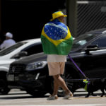 
              A man walks his dog, with a Brazilian national flag draped over his shoulders during general elections, in Sao Paulo, Brazil, Sunday, Oct. 2, 2022. (AP Photo/Andre Penner)
            