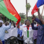 
              Demonstrators gather near Thomas Sankara memorial with Burkina Faso and Russian flags in support of what they believe to be another military coup in Ouagadougou Friday Sept. 30, 2022. Residents say gunfire rang out early in the morning and the state broadcaster has gone off the air, fueling fears that another coup is underway. The developments Friday come just after coup leader-turned-president Lt. Col. Paul Henri Sandaogo Damiba returned from a trip to the U.N. General Assembly. (AP Photo)
            