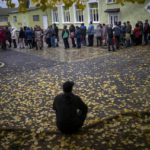 
              A man sits as people queue to receive a daily ration of bread in a school in Mykolaiv, Tuesday, Oct. 25, 2022. Mykolaiv residents pick up bread from the only food distribution point in Varvarivka, a Mykolaiv district where thousands of people live. One person is allowed to receive free bread just once in three days. (AP Photo/Emilio Morenatti)
            