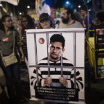 
              FILE - A woman holds a poster depicting Brazil's Justice Minister Sergio Moro behind bars, wearing a prison uniform, during a protest in Rio de Janeiro, Brazil, Thursday, Oct. 3, 2019. When Moro resigned to enter politics, many in Brazil believed the anti-corruption crusader who jailed a popular former president could someday occupy the nation’s most powerful office. But on the eve of Brazil’s Oct. 2 general election, the once-revered magistrate was fighting what polls showed was a losing battle for a Senate seat. (AP Photo/Silvia Izquierdo)
            