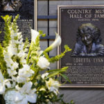 
              Flowers stand near the plaque of Loretta Lynn in the Country Music Hall of Fame Tuesday, Oct. 4, 2022, in Nashville, Tenn. Lynn, the Kentucky coal miner's daughter who became a pillar of country music, died Tuesday at her home in Hurricane Mills, Tenn. She was 90. (AP Photo/Mark Humphrey)
            