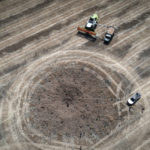 
              FILE - Next to a crater left by a Russian rocket, a farmer harvests a field 10 kilometers (6 miles) from the front line between Russian and Ukranian forces, in the Dnipropetrovsk region, Ukraine, Monday, July 4, 2022. (AP Photo/Efrem Lukatsky, File)
            