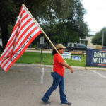 
              Dolly Schultz waves a flag outside of the town's main early voting location on the first day of early voting, Monday, Oct. 24, 2022, in Uvalde, Texas. The Uvalde school massacre has cast a long shadow in the midterm elections in Texas, intensifying Republican Gov. Greg Abbott’s reelection fight against Democrat Beto O’Rourke and driving a blitz of television ads.  (AP Photo/Acacia Coronado)
            