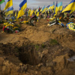 
              Ukrainian flags wave next to graves of recently killed Ukrainian servicemen in a cemetery during Ukraine Defenders Day in Kharkiv, Ukraine, Friday, Oct. 14, 2022. (AP Photo/Francisco Seco)
            