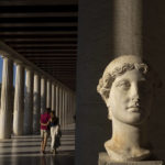 
              A young couple walk behind a 2nd century A.D. marble head of victory inside Stoa of Attalos, at ancient Agora, in Athens, on Monday, Oct. 3, 2022. Greece is on course to beat its annual record for tourism revenue as southern European Union members made a surprise recovery following a two-year travel slump caused by the pandemic. (AP Photo/Petros Giannakouris)
            
