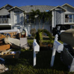 
              Darryl Hudson of Ontario, Canada, has a morning coffee on the damaged balcony of his vacation home, as water-damaged furniture, debris, and vehicles sit on the lawn after storm surge filled the first story of his and surrounding homes during the passage of Hurricane Ian, near San Carlos Boulevard in Fort Myers Beach, Fla., Sunday, Oct. 2, 2022. (AP Photo/Rebecca Blackwell)
            