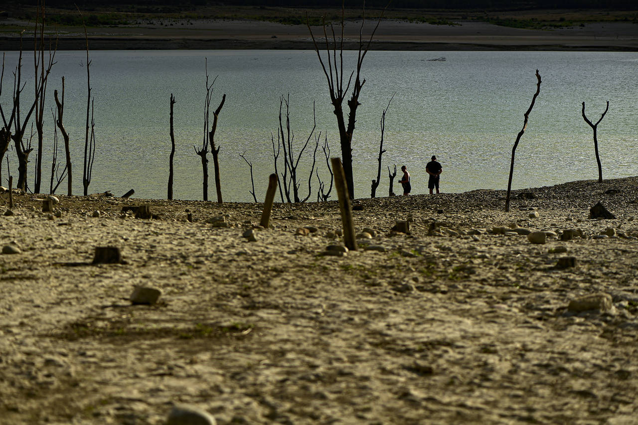 FILE - People walk close to the border at Yesa's reservoir affected by drought, on a sunny summer d...