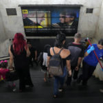 
              Commuters at a bus station walk below a screen showing Brazil's former President Luiz Inacio Lula da Silva, left, and current President  Jair Bolsonaro, both of whom are running for president, and the news that the previous day's election results have lead to a second round in Brasilia, Brazil, Monday, Oct. 3, 2022. The second round of the Brazilian elections takes place on Oct. 30. (AP Photo/Eraldo Peres)
            