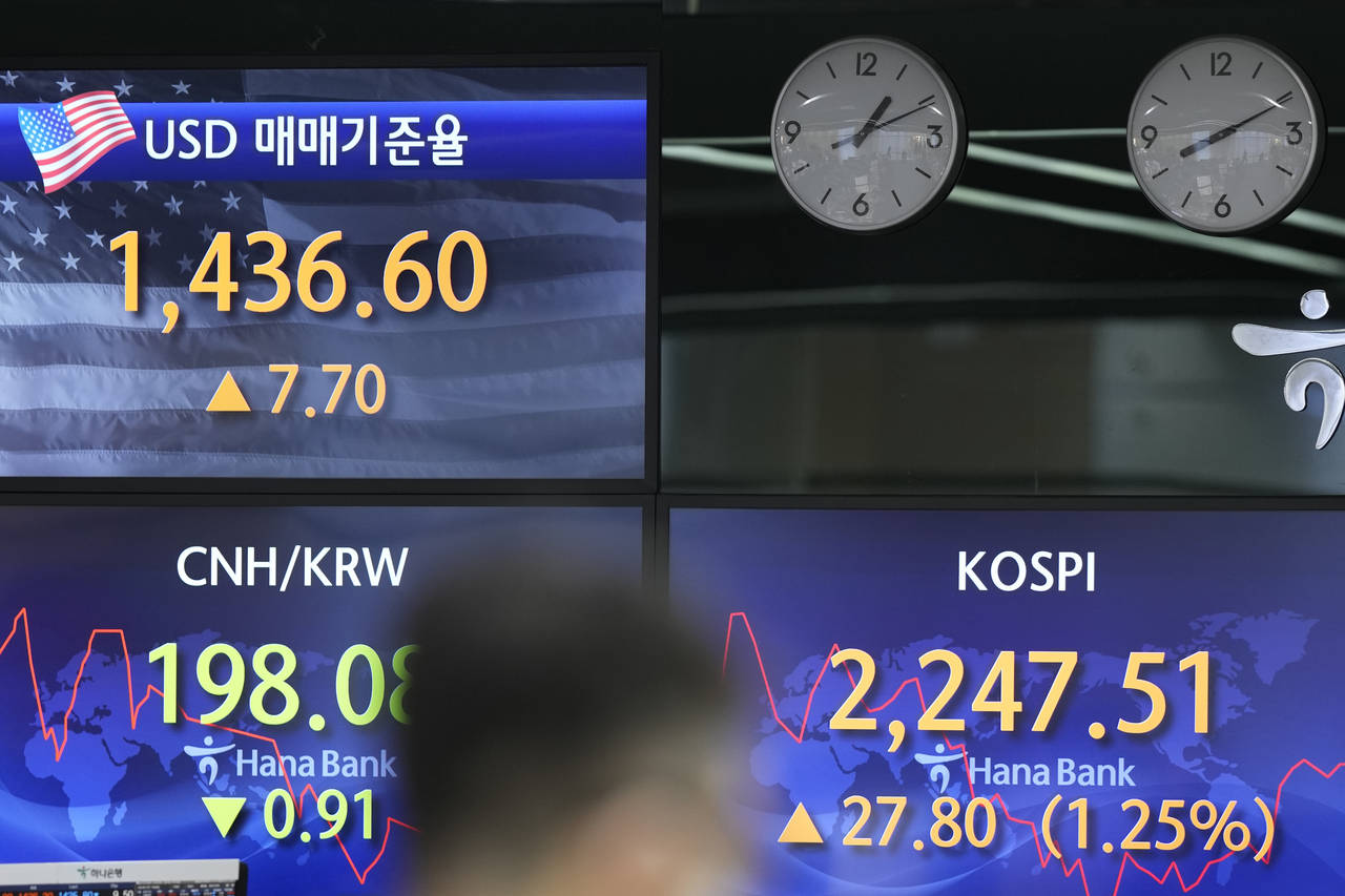 A currency trader walks by the screens showing the Korea Composite Stock Price Index (KOSPI), right...