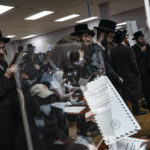 
              Poll workers are seen in a reflection while members of the Orthodox Jewish community register to collect ballot papers at a polling center on, Tuesday, Nov. 8, 2022, in the Brooklyn borough of New York. (AP Photo/Wong Maye-E)
            