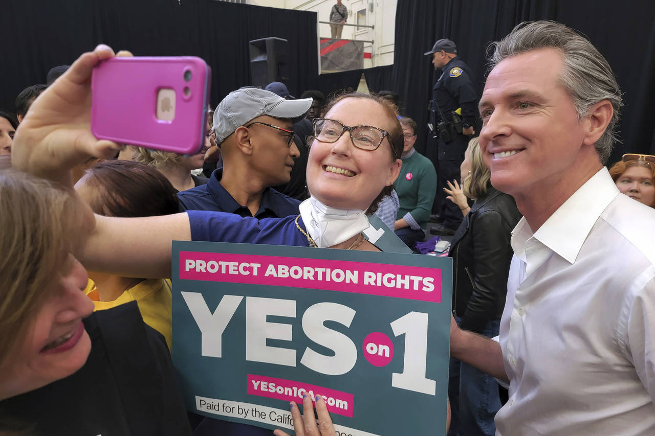 FILE -- California Gov. Gavin Newsom, right, takes selfies with supporters at a vote YES on Proposi...