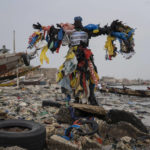 
              The environmental activist Modou Fall, who many simply call "Plastic Man", poses for a photo at the Yarakh Beach littered by trash and plastics in Dakar, Senegal, Tuesday, Nov. 8, 2022. As he walks, plastics dangle from his arms and legs, rustling in the wind while strands drag on the ground. On his chest, poking out from the plastics, is a sign in French that says, "No to plastic bags." (AP Photo/Leo Correa)
            