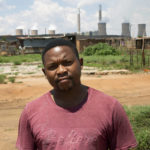 
              Selby Mahlalela poses for a photograph against the backdrop of the coal-powered Duvha power station, near Emalahleni (formerly Witbank) east of Johannesburg, Thursday, Nov. 17, 2022. Living in the shadow of one of South Africa’s largest coal-fired power stations, residents of Masakhane fear job losses if the facility is closed as the country moves to cleaner energy. (AP Photo/Denis Farrell)
            