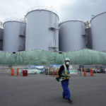 
              FILE - A worker helps direct a truck driver as he stands near tanks used to store treated radioactive water after it was used to cool down melted fuel at the Fukushima Daiichi nuclear power plant, run by Tokyo Electric Power Company Holdings (TEPCO), in Okuma town, northeastern Japan, Thursday, March 3, 2022. Repayment of the more than 10 trillion yen ($68 billion) government funding for cleanup and compensation for the Fukushima Daiichi nuclear plant disaster has been delayed the Board of Audit said in a report released Monday, Nov. 7, 2022. (AP Photo/Hiro Komae, File)
            
