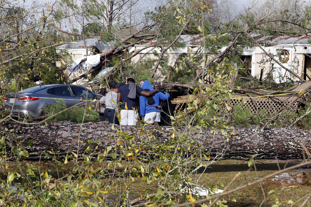Friends and family pray outside a damaged mobile home, Wednesday, Nov. 30, 2022, in Flatwood, Ala.,...