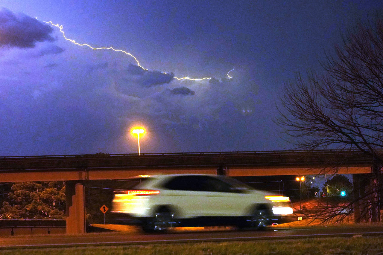 A vehicle races along a Jackson, Miss., street as lightning streaks across the sky, Tuesday evening...