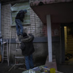 
              Two residents use food-packaging material to cover windows of a damaged building during a recent Russian strike while another resident lies inebriated at the entrance of a building in the southern city of Kherson, Ukraine, Sunday, Nov. 27, 2022. Shelling by Russian forces struck several areas in eastern and southern Ukraine overnight as utility crews continued a scramble to restore power, water and heating following widespread strikes in recent weeks, officials said Sunday. (AP Photo/Bernat Armangue)
            