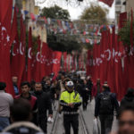 
              A police officer stands as other people walk in the decorated with Turkish flags Istanbul's popular pedestrian Istiklal Avenue in Istanbul, Monday, Nov. 14, 2022. Turkish police said Monday that they have detained a Syrian woman with suspected links to Kurdish militants and that she confessed to planting a bomb that exploded on a bustling pedestrian avenue in Istanbul, killing six people and wounding several dozen others.(AP Photo/Khalil Hamra)
            