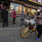 
              A resident wearing a mask pushes a bicycle with her groceries past a store controlling the flow of shoppers in Beijing, Friday, Nov. 25, 2022. Residents of China's capital were emptying supermarket shelves and overwhelming delivery apps Friday as the city government ordered accelerated construction of COVID-19 quarantine centers and field hospitals. (AP Photo/Ng Han Guan)
            