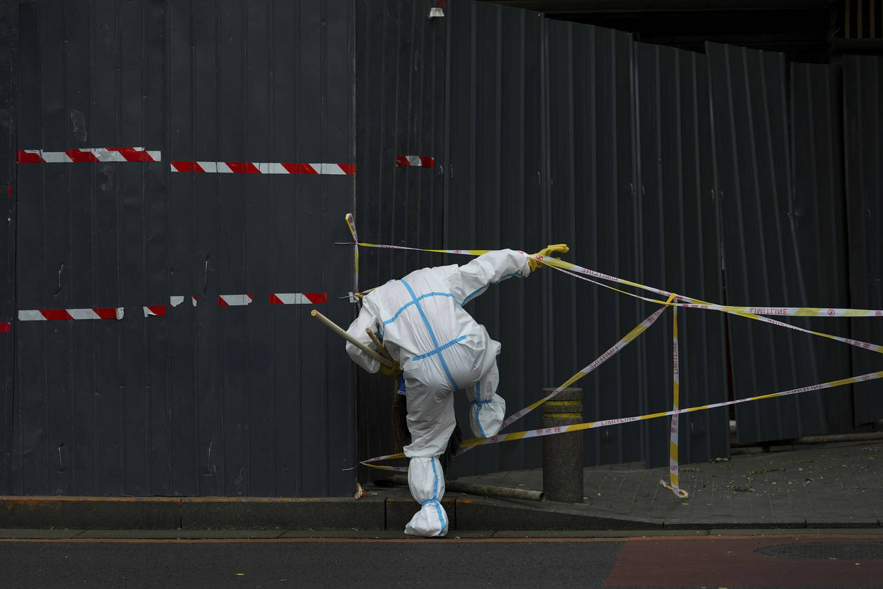 FILE - A worker in protective suit walks through the caution tapes along metal barricades retail sh...