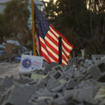 A signs promoting a candidate for Fort Myers Beach town council sits amid debris near an American Flag, along a roadside on Estero Island, which was heavily damaged in September's Hurricane Ian, in Fort Myers Beach, Fla, Tuesday, Nov. 8, 2022. After the area was devastated and thousands were left displaced by Hurricane Ian, Lee County extended their early voting period and permitted voters on Election Day to cast their ballot in any of the dozen open polling places. (AP Photo/Rebecca Blackwell)