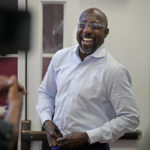 
              Democratic nominee for U.S Senate Sen. Raphael Warnock laughs as he buttons his shirt to hide a microphone cord before speaking the the media at a campaign stop on the campus of Morehouse College Tuesday, Nov. 8, 2022, in Atlanta. (AP Photo/John Bazemore)
            