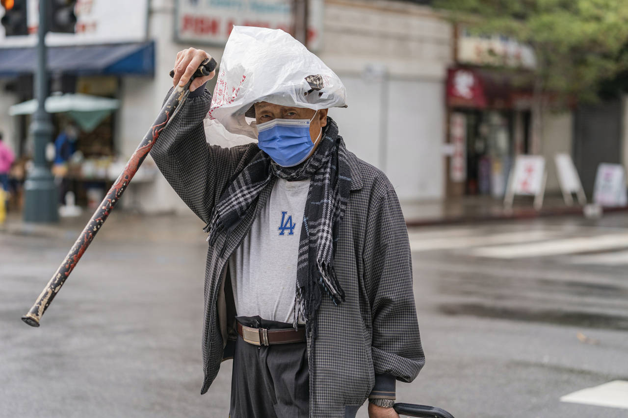 A pedestrian protects his hat from the rain with a plastic bag in the Chinatown district of Los Ang...