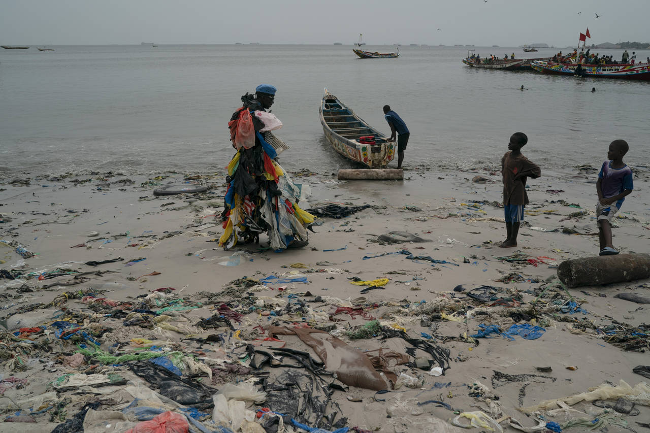 Kids look at environmental activist Modou Fall, who many simply call "Plastic Man", while he walks ...