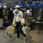 
              A resident carries her groceries near cashier machines at a supermarket in Beijing, Friday, Nov. 25, 2022. Residents of China's capital were emptying supermarket shelves and overwhelming delivery apps Friday as the city government ordered accelerated construction of COVID-19 quarantine centers and field hospitals. (AP Photo/Ng Han Guan)
            
