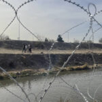 
              A family is seen on the Mexican side of the Rio Grande River through the concertina wire placed earlier in the day by Texas National Guard troops at site of the recent mass migrant crossings in El Paso, Texas, Tuesday, Dec. 20, 2022. (AP Photo/Giovanna Dell'Orto)
            