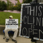 
              FILE -  An anti-abortion supporter sits behind a sign that advises the Jackson Women's Health Organization clinic is still open in Jackson, Miss., Wednesday, July 6, 2022. (AP Photo/Rogelio V. Solis, File)
            