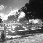FILE - In this photo provided by the U.S. Navy, U.S. sailors stand among wrecked airplanes at Ford Island Naval Air Station as they watch the explosion of the USS Shaw in the background, during the Japanese attack on Pearl Harbor, Hawaii, Dec. 7, 1941. In December 2022, the U.S. Navy and the National Park Service will host a remembrance ceremony at Pearl Harbor on the 81st anniversary of the 1941 Japanese bombing. (U.S. Navy via AP, File)
