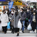 
              People with shopping bags walk across a traffic intersection towards a train station near a shopping street in the Ueno district famous for a year-end shopping before New Year holidays in Tokyo, Friday, Dec. 30, 2022. (AP Photo/Hiro Komae)
            