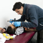 
              Dr. Brian Elmore, right, with the Texas Tech University Health Sciences Center in El Paso, Texas, checks the bleeding nose of Honduran migrant Elvin Cruz, 5, as his mother, Diana Rosales, looks on at a government-run shelter in Ciudad Juarez, Mexico, on Sunday, Dec. 18, 2022. (AP Photo/Andres Leighton)
            