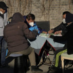 
              Residents wearing masks play mahjong outdoor during a sunny day in Beijing, Tuesday, Dec. 27, 2022. China is on a bumpy road back to normal life as schools, shopping malls and restaurants fill up again following the abrupt end of some of the world's most severe restrictions even as hospitals are swamped with feverish, wheezing COVID-19 patients. (AP Photo/Ng Han Guan)
            