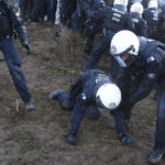 
              A police officers helps a colleague as police scuffle with demonstrators at village Luetzerath near Erkelenz, Germany, Tuesday, Jan. 10, 2023. The village of Luetzerath is occupied by climate activists fighting against the demolishing of the village to expand the Garzweiler lignite coal mine near the Dutch border. Poster read: „1,5 degrees celsius means: Luetzerath stays". (AP Photo/Michael Probst)
            