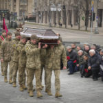 
              People kneel as the Ukrainian servicemen carry the coffin of their comrade Oleh Yurchenko killed in a battlefield with Russian forces in the Donetsk region during a commemoration ceremony in Independence Square in Kyiv, Ukraine, Sunday, Jan. 8, 2023. (AP Photo/Efrem Lukatsky)
            