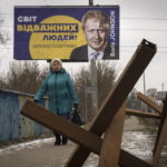 
              A woman passes by a board depicting former British Prime Minister Boris Johnson and reads: "The World of Brave People! #thank you for support", with antitank hedgehogs in the foreground, in the town of Bucha, outside Kyiv, Ukraine, Monday Jan. 30, 2023. (AP Photo/Efrem Lukatsky)
            