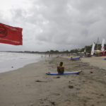 
              A man sits on a surfboard at Kuta beach on the popular tourist island of Bali, Indonesia, Thursday, Jan. 19, 2023. A hoped-for boom in Chinese tourism in Asia over next week's Lunar New Year holidays looks set to be more of a blip as most travelers opt to stay inside China if they go anywhere. (AP Photo/Firdia Lisnawati)
            