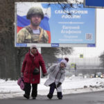 
              A woman and a girl walk past a billboard with a portrait of a Russian officer awarded for action in Ukraine and the words "Glory to the heroes of Russia" in St. Petersburg, Russia, Wednesday, Jan. 11, 2023. (AP Photo/Dmitri Lovetsky)
            