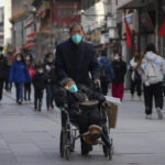 
              An elderly man wearing a face mask pushes his partner in a wheelchair as visitors tour a pedestrian shopping street at Qianmen, in Beijing, Tuesday, Jan. 3, 2023. As the virus continues to rip through China, global organizations and governments have called on the country start sharing data while others have criticized its current numbers as meaningless. (AP Photo/Andy Wong)
            
