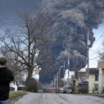 
              A man takes photos as a black plume rises over East Palestine, Ohio, as a result of a controlled detonation of a portion of the derailed Norfolk Southern trains Monday, Feb. 6, 2023. (AP Photo/Gene J. Puskar)
            