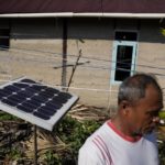 
              A man walks past a small solar panel he uses for back up, outside his house on Karampuang Island, in West Sulawesi, Indonesia, Thursday, Dec. 22, 2022. While Indonesia has vast renewable and green energy potential from solar, wind, geothermal and other sources, experts warn that the vast archipelago nation faces unique financial, policy, infrastructure and other challenges that will require innovation. (AP Photo/Dita Alangkara)
            