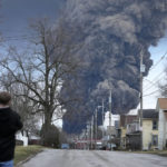 
              A man takes photos as a black plume rises over East Palestine, Ohio, as a result of a controlled detonation of a portion of the derailed Norfolk and Southern trains Monday, Feb. 6, 2023. (AP Photo/Gene J. Puskar)
            