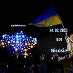 
              A Ukrainian protestor living in Cyprus, waves a flag of Ukraine as others stand in front of a screen during a protest marking the first anniversary of Russia's invasion of Ukraine, in capital Nicosia, Cyprus, on Friday, Feb 24, 2023. (AP Photo/Petros Karadjias)
            
