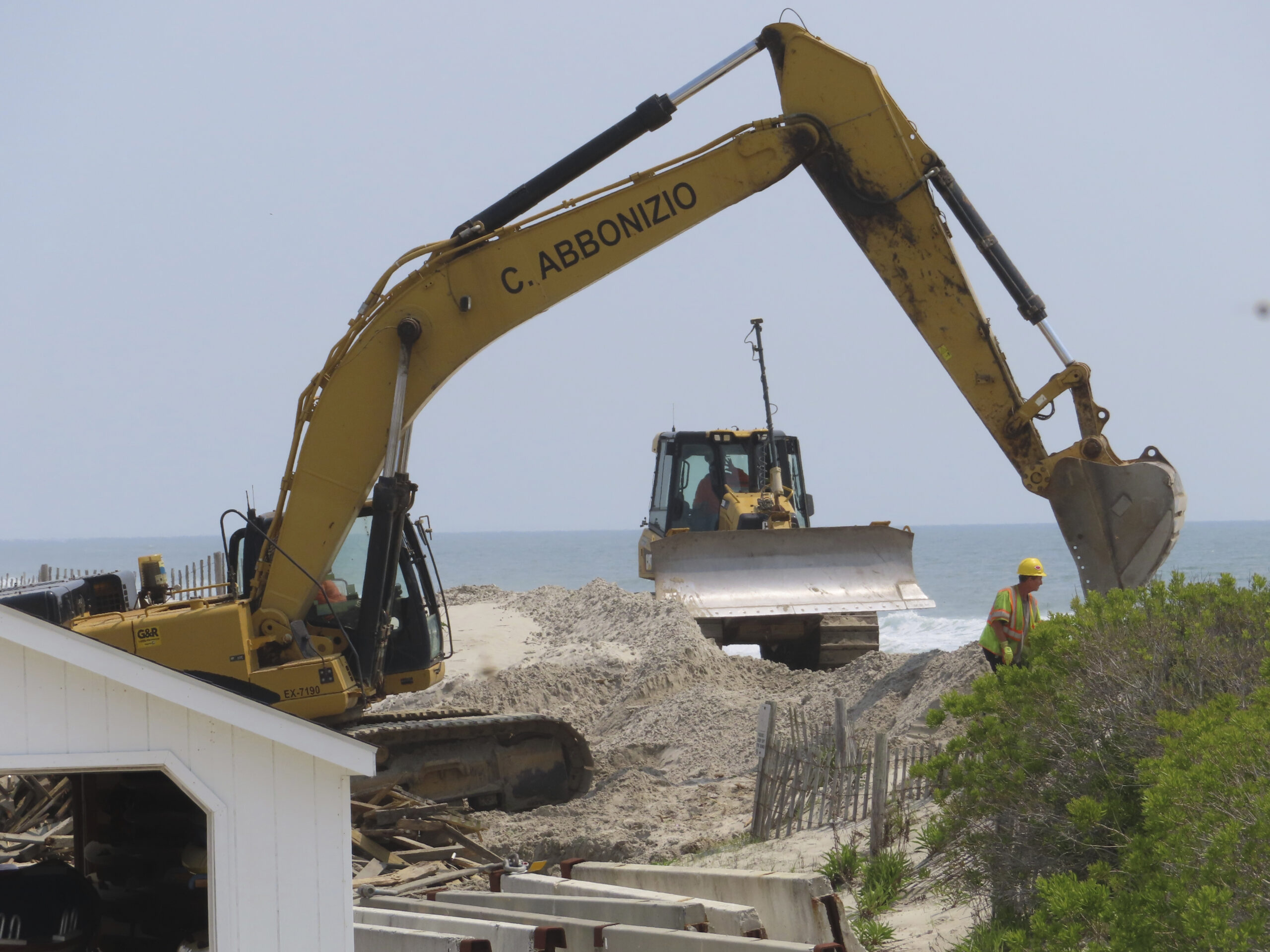 Heavy equipment operators remove old dune fencing and other debris from a badly eroded section of b...